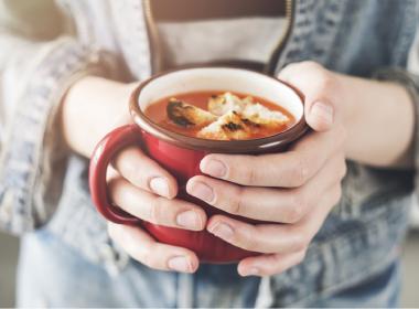 woman holding cup of soup with croutons in both hands